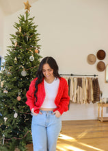 Load image into Gallery viewer, model wearing the where the heart is sweater in the color red. model has the sweater paired with a pair of light wash denim and is posing in front of a Christmas tree.