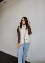 Load image into Gallery viewer, model wearing the long way home puffer in the color ecru. model has the vest paired with the can&#39;t get enough top in the color brown and a pair of light wash denim.