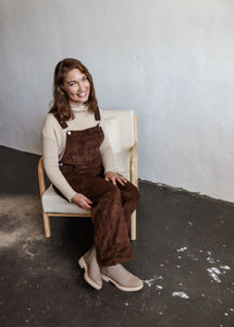 model wearing the settlin' down corduroy overalls in the color brown. model has the overalls paired with the by your side top in the color taupe and a pair of neutral boots.