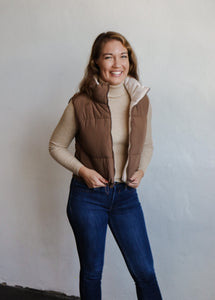 model wearing the vest of both worlds puffer in the color brown/cream. model has the vest paired with the can't get enough top in the color oatmeal and a pair of dark wash denim.