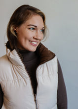 Load image into Gallery viewer, model wearing the vest of both worlds puffer in the color brown/cream. model has the vest paired with the can&#39;t get enough top in the color brown and a pair of dark wash denim.