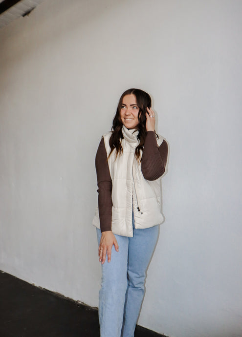 model wearing the long way home puffer in the color ecru. model has the vest paired with the can't get enough top in the color brown and a pair of light wash denim.