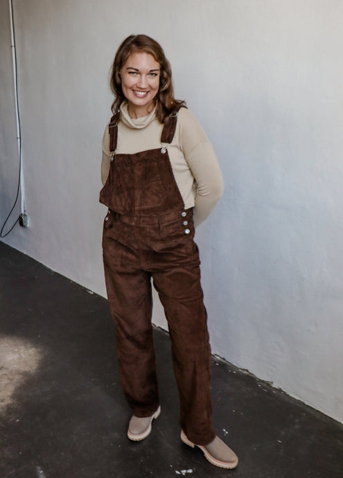 model wearing the settlin' down corduroy overalls in the color brown. model has the overalls paired with the by your side top in the color taupe and a pair of neutral boots.
