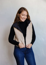 Load image into Gallery viewer, model wearing the vest of both worlds puffer in the color black/taupe. model has the vest paired with the can&#39;t get enough top in the color black and a pair of dark wash denim.