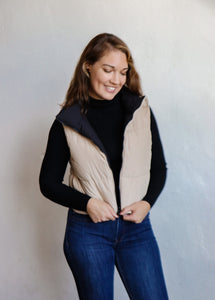 model wearing the vest of both worlds puffer in the color black/taupe. model has the vest paired with the can't get enough top in the color black and a pair of dark wash denim.