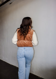 model wearing the seems so simple vest in the color camel. model has the vest paired with the every moment sweater in the color ivory and a pair of light wash denim.