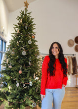 Load image into Gallery viewer, model wearing the my way back home sweater in the color red. model has the sweater paired with a pair of light wash denim and is posing in front of a Christmas tree.