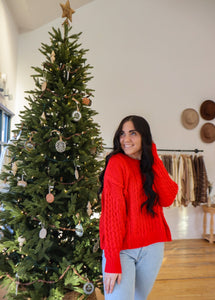 model wearing the my way back home sweater in the color red. model has the sweater paired with a pair of light wash denim and is posing in front of a Christmas tree.