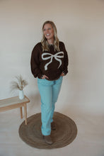 Load image into Gallery viewer, front view of model wearing the ribbons + bows sweater in the color chocolate. model has the sweater paired with the charleston denim.