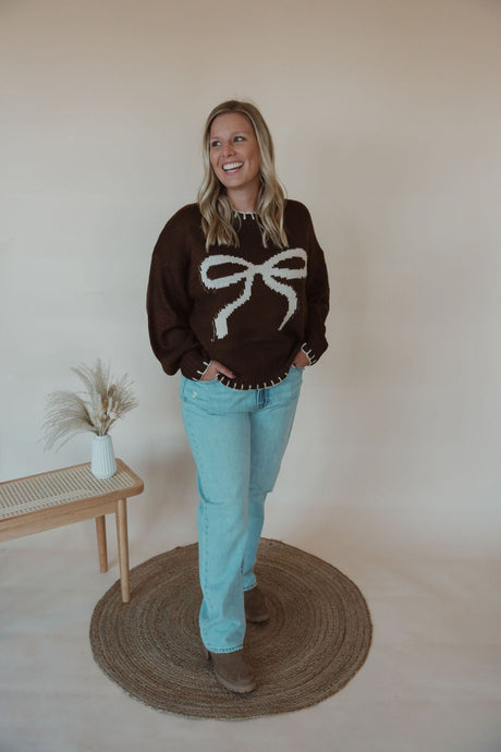 front view of model wearing the ribbons + bows sweater in the color chocolate. model has the sweater paired with the charleston denim.