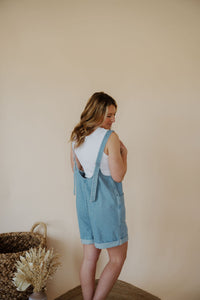 back view of model wearing the carly denim romper. model has the romper paired with the forever yours top in the color white.