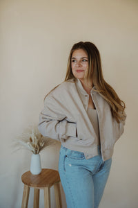 front view of model wearing the winding roads bomber jacket in the color light taupe. model has the jacket paired with the used to know bodysuit in the color biscuit and the charleston denim.