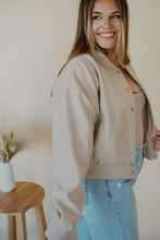 Load image into Gallery viewer, side view of model wearing the winding roads bomber jacket in the color light taupe. model has the jacket paired with the used to know bodysuit in the color biscuit and the charleston denim.
