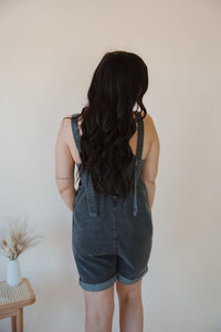 back view of model wearing the carly denim romper in the color charcoal. model has the romper paired with the these days top in the color charcoal.