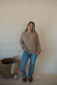 front view of model wearing the patiently waiting sweater in the color oat. model has the sweater paired with the aurora denim.