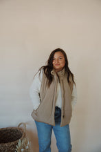 Load image into Gallery viewer, front view of model wearing the long way home puffer vest in the color mocha. model has the vest paired with the play it cool sweater and the aurora denim.