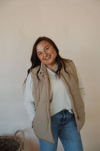 front view of model wearing the long way home puffer vest in the color mocha. model has the vest paired with the play it cool sweater and the aurora denim.