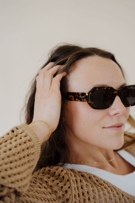 model wearing the onyx sunglasses in the color dark tortoise. model has the sunglasses paired with the ocean avenue cardigan in the color taupe and the forever yours top in the color white.