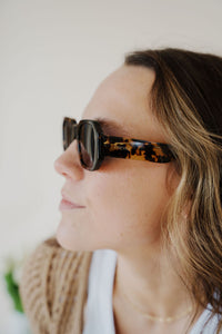 model wearing the onyx sunglasses in the color dark tortoise. model has the sunglasses paired with the ocean avenue cardigan in the color taupe and the forever yours top in the color white.