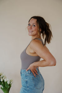 side view of model wearing the change your mind bodysuit in the color smoky taupe. model has the top paired with the austin denim shorts and the anna necklace.