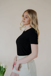 side view of model wearing the take a chance bodysuit in the color black. model has the top paired with the parker shorts and the dainty mallory necklace.