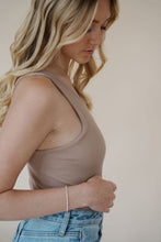 Load image into Gallery viewer, close side view of model wearing the change your mind bodysuit in the color light sand. model has the top paired with the genevieve denim and the dainty mallory necklace.