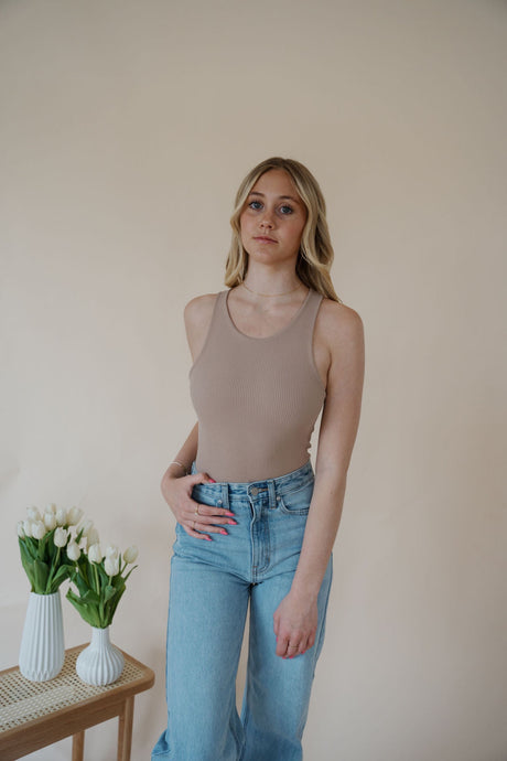 front view of model wearing the change your mind bodysuit in the color light sand. model has the top paired with the genevieve denim and the dainty mallory necklace.