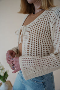 detail view of model wearing the ocean avenue cardigan in the color cream. model has the cardigan paired with the forever yours top in the color macchiato and the austin denim shorts.