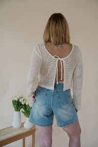 back view of model wearing the ocean avenue cardigan in the color cream. model has the cardigan paired with the forever yours top in the color macchiato and the austin denim shorts.