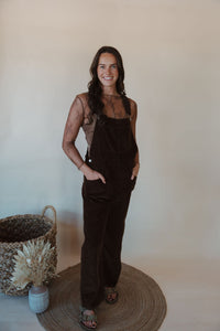 front view of model wearing the settlin' down corduroy overalls in the color brown. model has the overalls paired with the here to stay top in the color brown.