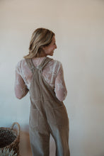 Load image into Gallery viewer, back view of model wearing the settlin&#39; down corduroy overalls in the color taupe. model has the overalls paired with the here to stay top in the color cream.