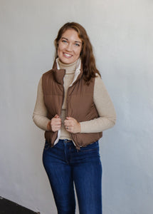 model wearing the vest of both worlds puffer in the color brown/cream. model has the vest paired with the can't get enough top in the color oatmeal and a pair of dark wash denim.