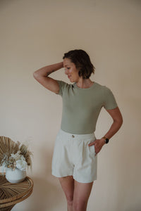front view of model wearing the take a chance bodysuit in the color soft olive. model has the bodysuit paired with the making promises shorts.