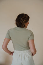 Load image into Gallery viewer, back view of model wearing the take a chance bodysuit in the color soft olive. model has the bodysuit paired with the making promises shorts.