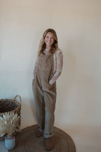 front view of model wearing the settlin' down corduroy overalls in the color taupe. model has the overalls paired with the here to stay top in the color cream.