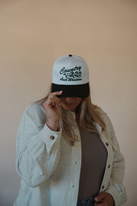 front view of model wearing the country and western trucker hat. model has the hat paired with the never be the same shacket and the change your mind bodysuit in the color smoky taupe.