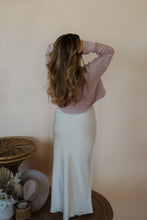 Load image into Gallery viewer, back view of model wearing the cherish satin maxi in the color ivory. model has the skirt paired with the devoted sweater.