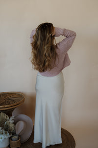 back view of model wearing the cherish satin maxi in the color ivory. model has the skirt paired with the devoted sweater.