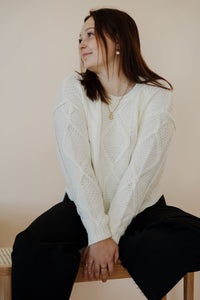 front view of model wearing the somewhere in the middle sweater in the color ivory. model has the sweater paired with the addison denim in the color fade black.