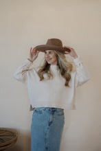 Load image into Gallery viewer, front view of model wearing the halfway there sweater in the color cream. model has the sweater paired with the as long as I live denim midi skirt and a wide brim hat.