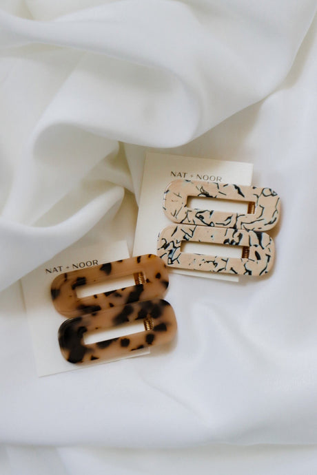 ophelia barrettes in the colors tortoise and marble. barrettes are shown attached to an accessory card laid on top of a white sheet.