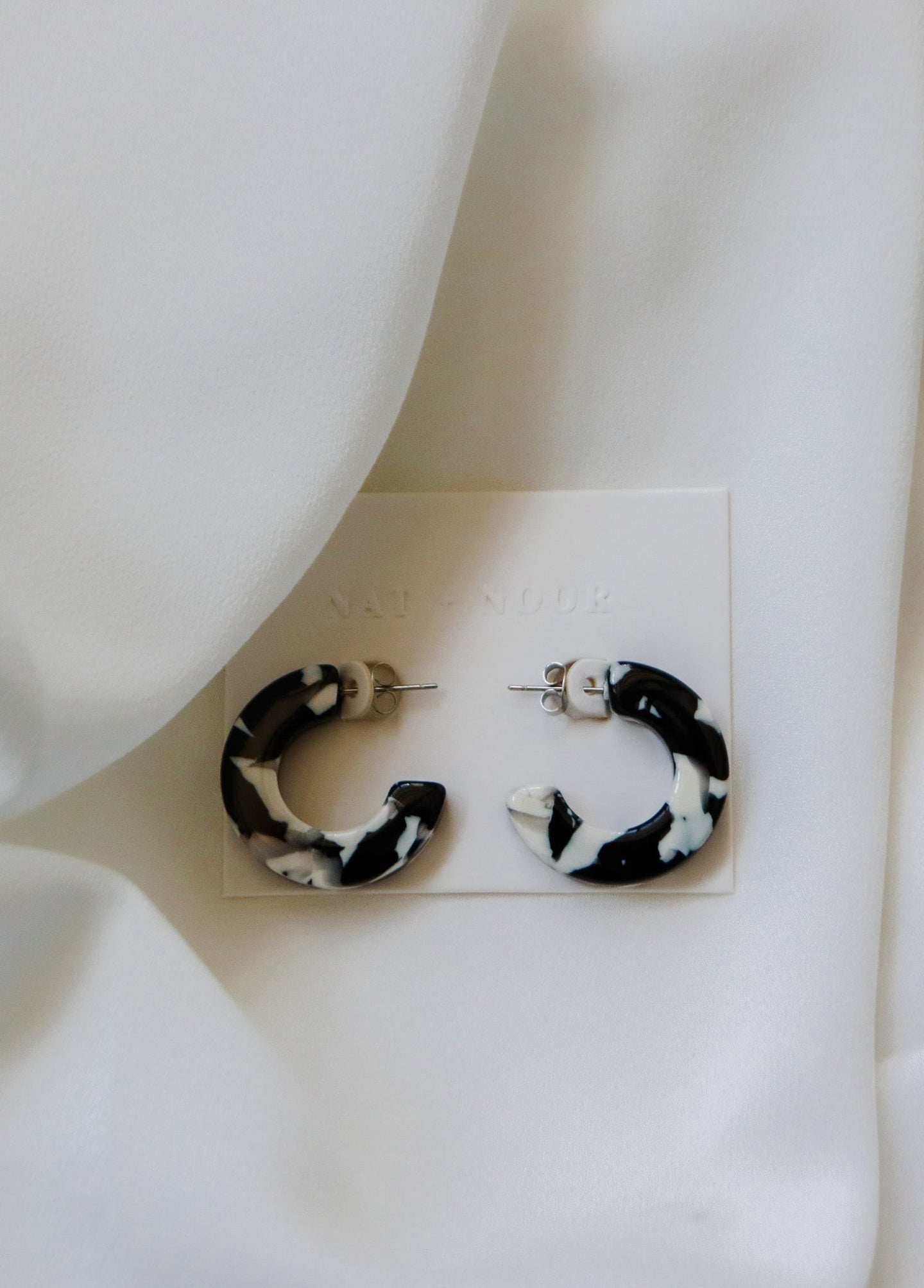felicity hoop earrings in the color black + white. earrings are shown on an earring card laid on top of a white sheet.
