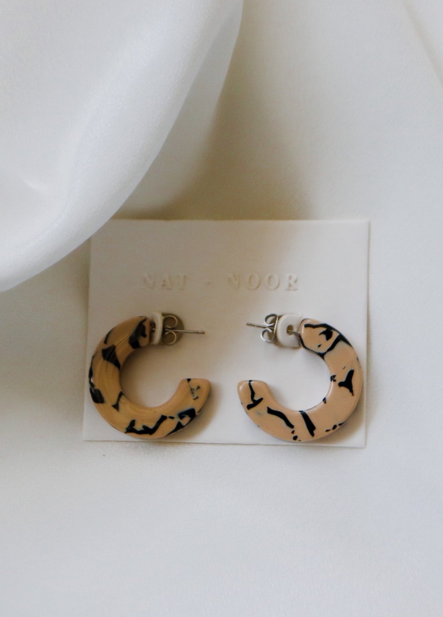 felicity hoop earrings in the color marble. earrings are shown on an earring card laid on top of a white sheet.