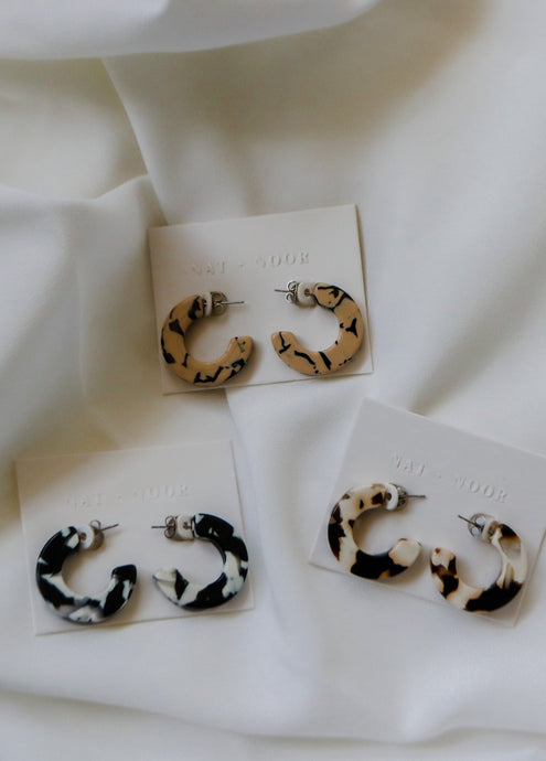 felicity hoop earrings in black + white, marble, and coco cream. earrings are shown laid out on earring cards on top of a white sheet.