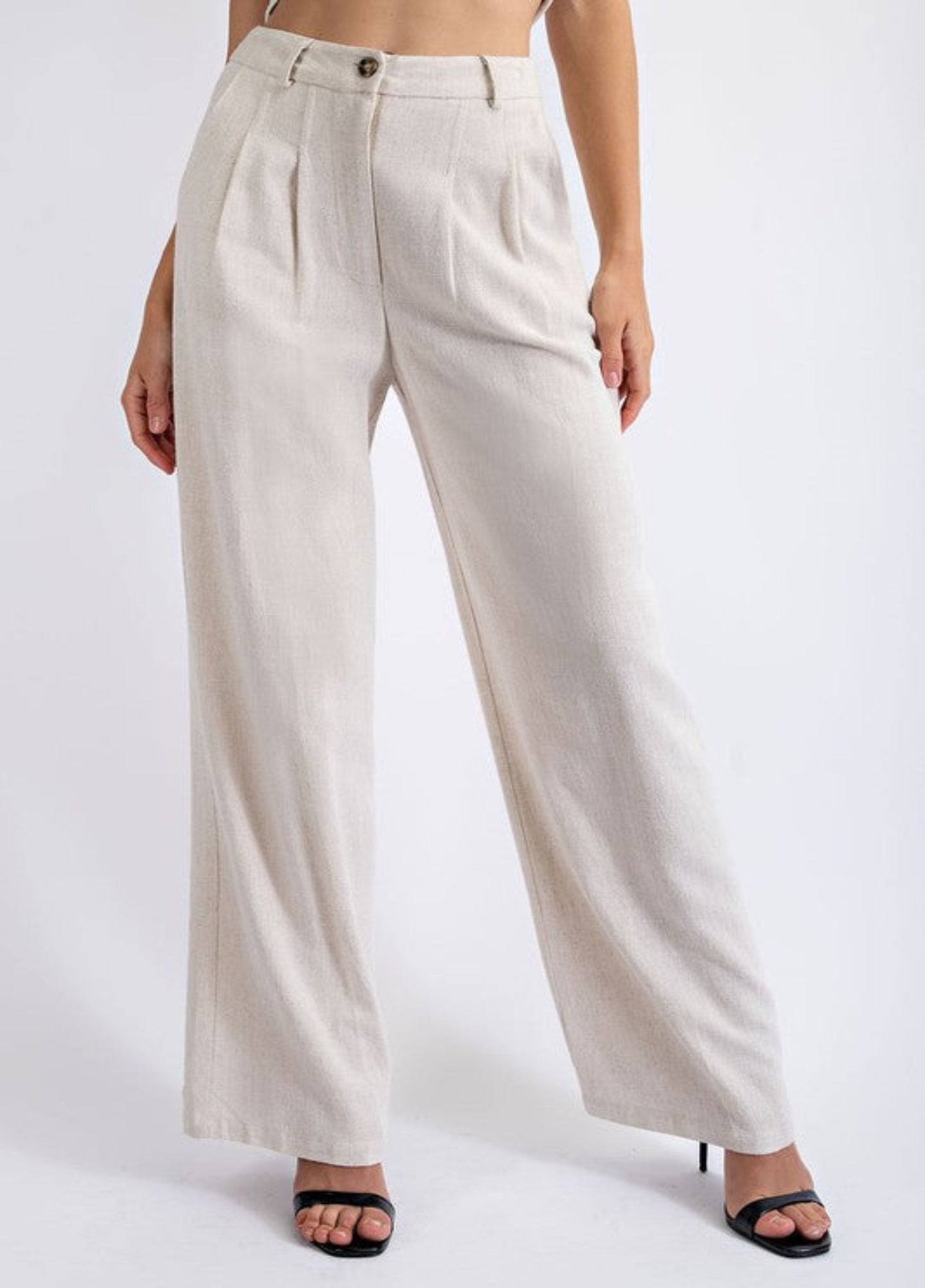 Photo of model wearing the Chelsea Linen Trousers in the color Oatmeal paired with black heels. Photo is taken from the torso down.