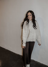 Load image into Gallery viewer, model wearing the late night talking sweater in the color oatmeal. model has the sweater paired with the logan trousers in the color espresso + a pair of platform sneakers.