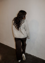 Load image into Gallery viewer, back view of model wearing the late night talking sweater in the color oatmeal. model has the sweater paired with the logan trousers in the color espresso + a pair of platform sneakers.