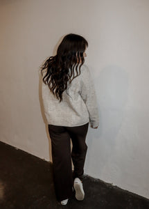 back view of model wearing the late night talking sweater in the color oatmeal. model has the sweater paired with the logan trousers in the color espresso + a pair of platform sneakers.