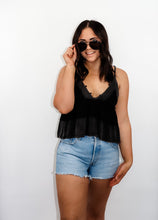 Load image into Gallery viewer, model wearing the moving on top in the color black paired with light denim shorts; model is wearing a pair of sunglasses and has one hand pinching the frames