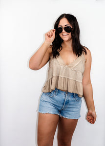 model wearing the moving on top in the color taupe paired with light denim shorts; model is wearing a pair of sunglasses with one hand pinching the frames